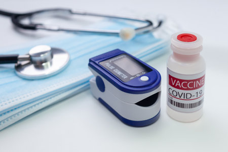 Medical concept. Pulse oximeter and COVID 19 vaccine vial. Selective focus.