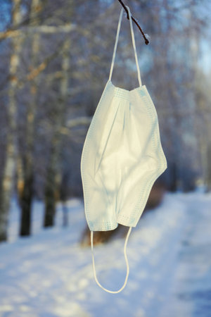 Used medical mask hanging on a tree branch, winter