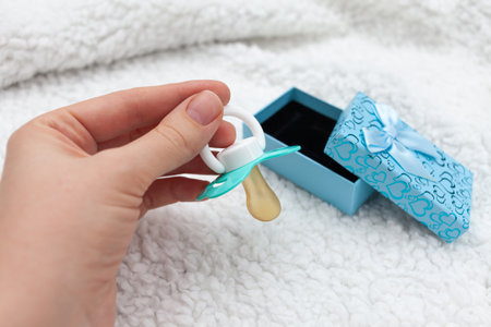 Woman's hand takes a blue pacifier from a gift box