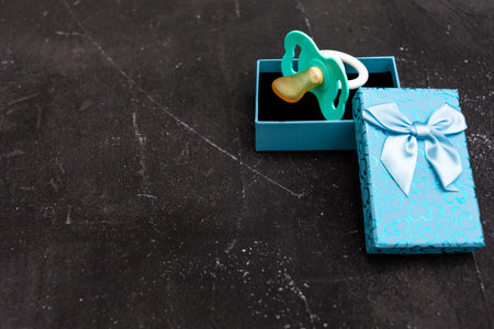 Gift box and pacifier for little boy on black background