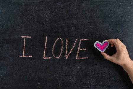 The inscription "I LOVE" on the chalk board. Hand with heart symbolの写真素材