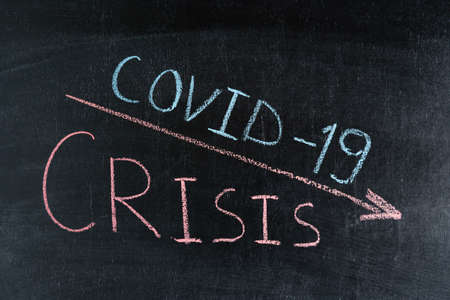CRISIS and COVID 19 word written in red chalk and downward arrow on chalk boardの写真素材