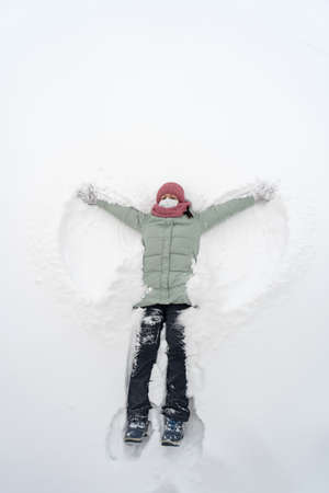 A girl in a medical mask is lying in the snow. Snow angelの写真素材