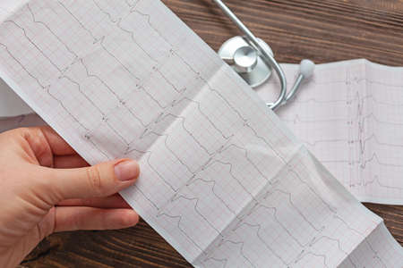 Doctor examining cardiogram on background stethoscope and wooden backgroundの写真素材