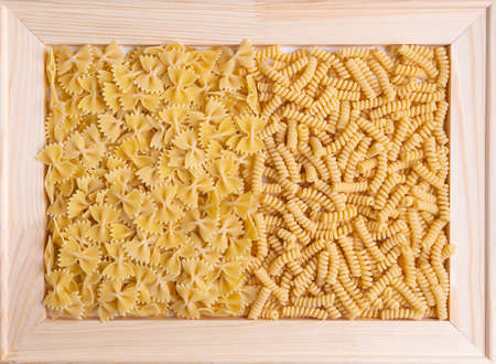 Farfalle and fusilli pasta in a wooden frame. Top viewの写真素材