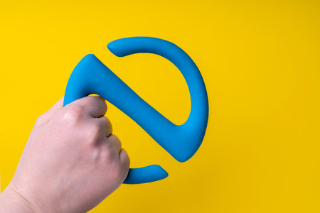 S-shaped gymnastic dumbbell in a female hand on a yellow background