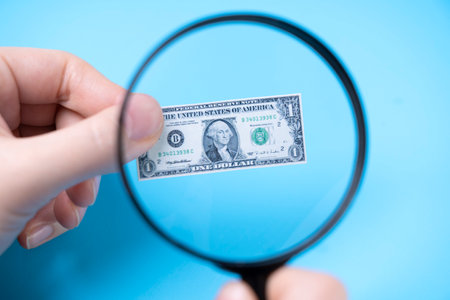 Hand with a magnifying glass looks at a small dollar on a blue background
