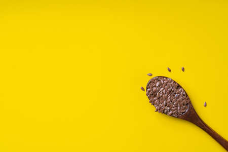 Dry flax seeds in a dark wooden spoon on a yellow background