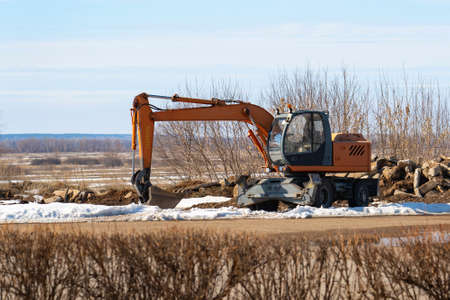 An orange excavator on the side of the road in the spring.