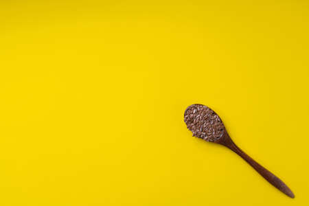 Fresh flax seeds in a dark wooden spoon on a yellow background