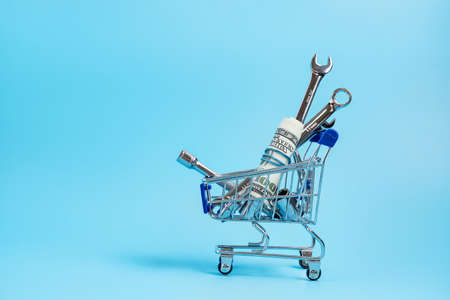 supermarket trolley with dollars, wrenches and other auto tools on blue backgroundの写真素材