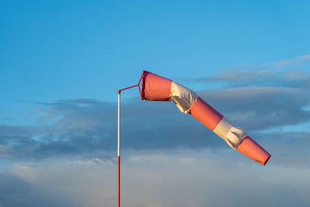 Red and white wind indicator in the shape of a cone at the airfield. Sunset and clouds in the backgroundの写真素材