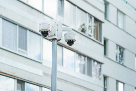 Surveillance cameras located on a pole, the facade of an apartment building in the background.