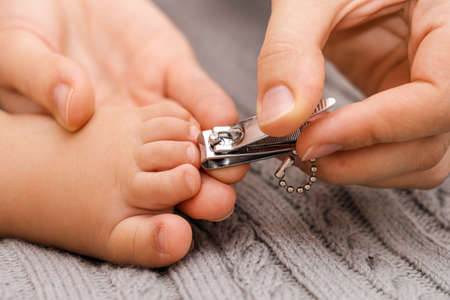 Hands of a mother cutting nails on the bare foot of a baby, close-up. Selective focusの写真素材
