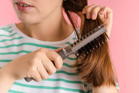 Brunette combs her long hair with a massage hair brush, close-up on a pink backgroundの写真素材