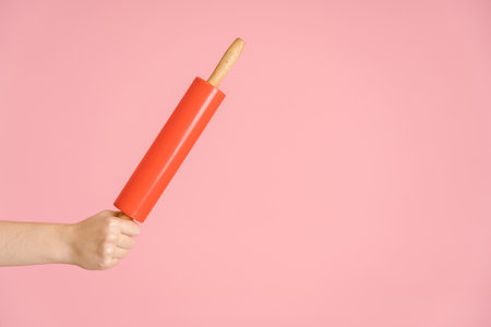 Rolling pin in a woman's hand on a pink background, copyspaceの写真素材