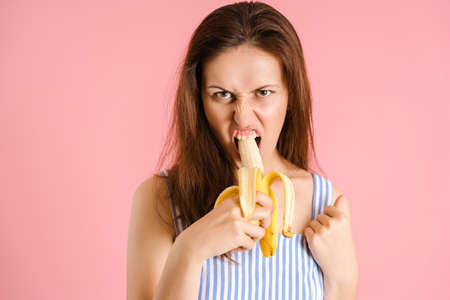 A very hungry sexy brunette aggressively bites a banana on a pink backgroundの写真素材