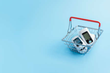 The device is a pulse oximeter in a miniature supermarket cart on a blue background. Copyspace
