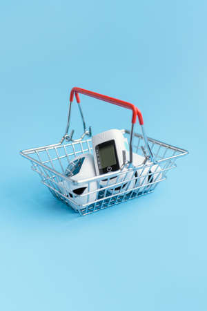 The device is a pulse oximeter in a miniature supermarket cart on a blue background. Vertical fotoの写真素材