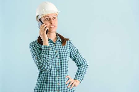 A female engineer in a white helmet is talking on the phone standing on a blue backgroundの写真素材