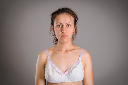 A young adult woman is depressed after giving birth. A woman on a gray dark background in a bra for breastfeeding babies.の写真素材