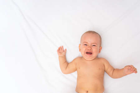 Hungry baby crying lying in bed on a white sheet, top view. Copyspaceの写真素材