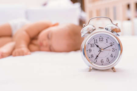 Bedtime. Alarm clock on the bed next to the sleeping newborn. Selective focus on the clock.の写真素材