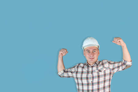 Handsome strong man builder in a white helmet on a blue background, Copyspaceの写真素材