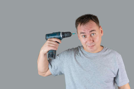A man in a gray T-shirt holding a screwdriver at his head like a weapon on a gray background.の写真素材