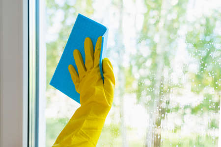 Window glass washing. A hand in a yellow glove washes the window with a blue rag
