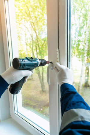 A man installs a white plastic handle on the window with an electric screwdriver