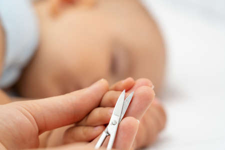 Cutting nails of a sleeping baby. Mom cuts the fingernails of her newborn daughter while sleeping, close-up. Selective focusの写真素材