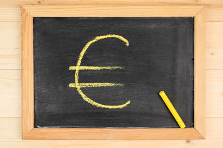 Drawing of the Euro symbol on a black chalk board in a frame, yellow chalk. Top viewの写真素材