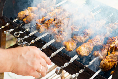 Pork shashlik on metal skewers. Smoke from burning fat. Man handの写真素材
