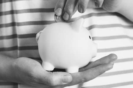 A woman puts a coin in a pink piggy bank, black and white photo, close-up