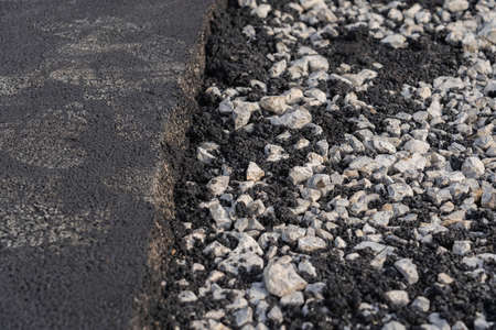 New asphalt pavement on one of the lanes of the road, gravel on the other lane of the road before laying asphaltの写真素材