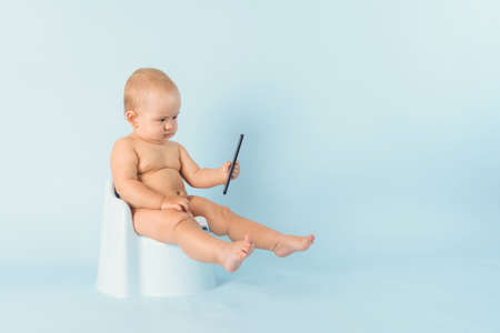 A baby aged 12-17 months is sitting on a potty with a smartphone. The concept of people's dependence on gadgets and social networks, copyspaceの写真素材