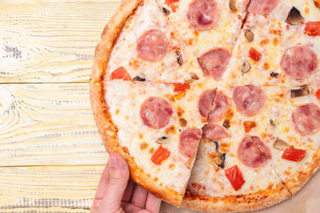 A woman's hand takes a piece of hot capriccioso pizza, top viewの写真素材