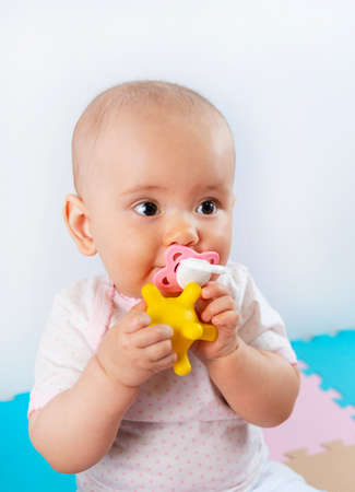 Newborn baby with a pacifier in his mouth holds a yellow rubber ball in his handsの写真素材