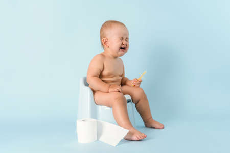 A small child is sitting on a potty and crying. Diarrhea and bloating in a newborn.の写真素材