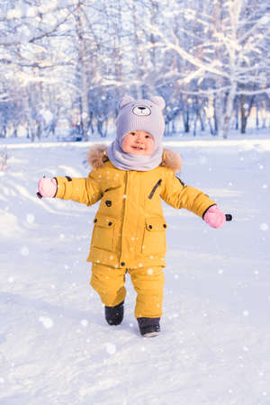 A happy baby in winter clothes enjoys the snow while walking in a winter parkの写真素材
