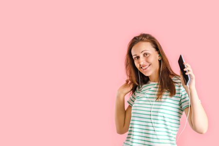 A beautiful brunette is smiling and dancing while listening to music with headphones through an app in her smartphone.の写真素材