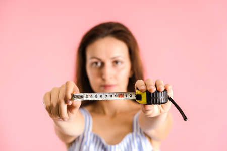 a young adult brunette holds a measuring tape in her hands, hinting at the small size of the penis. Studio shot on a pink background, selective focusの写真素材