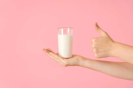 A hand with a glass of milk on a pink background. A glass with a dairy product on an open palm and a hand making a gesture classの写真素材