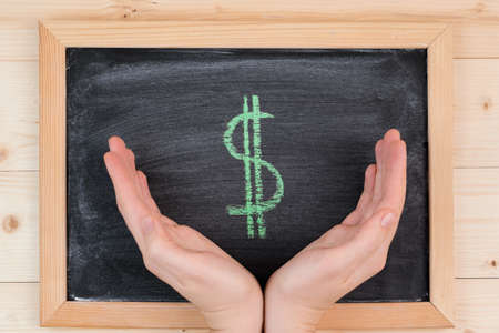 women's palms embrace the green dollar symbol on a chalkboard, top viewの写真素材