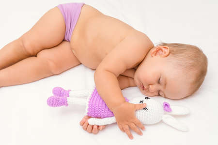 A beautiful newborn baby 12-17 months old is sleeping hugging a knitted rabbit toy.の写真素材