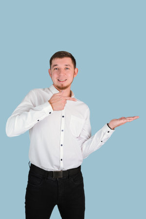 A bearded man 25-29 years old in a white shirt makes an index gesture to an open palm while standing on a blue background, vertical photoの写真素材