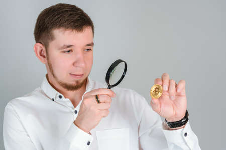 A businessman studies a bitcoin gold coin with a magnifying glassの写真素材