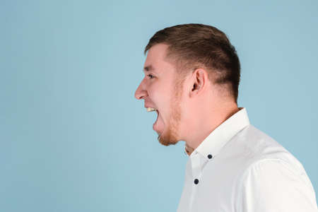 A bearded man shouts with his mouth open portrait in profile on a blue backgroundの写真素材