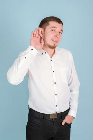 A bearded man holds his palm near his ear and listens attentively while standing on a blue backgroundの写真素材